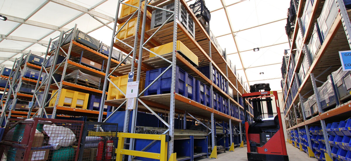 Warehouse with items stacked on shelving and a Moffatt, within a spaciotempo temporary building